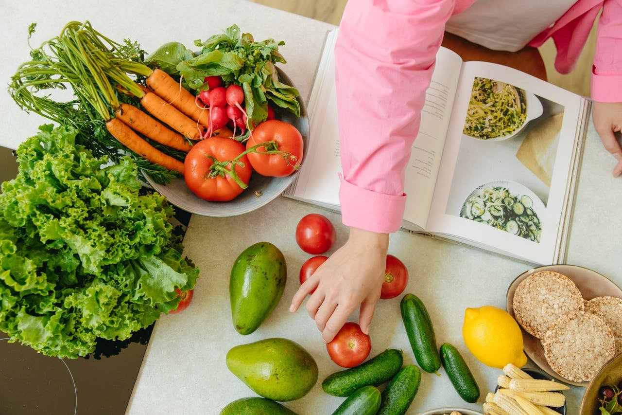 creative-01 Top view of fresh vegetables and hands arranging them with a recipe book, promoting healthy eating.
